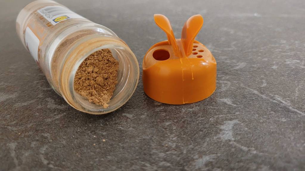 Getestet: Zimtpulver in einer transparenten Dose, die neben der orangefarbenen Dosierkappe liegt.