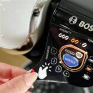 Eine Schutzfolie wird von der Bedienoberfläche der Bosch Tassimo My Way 2 abgezogen. Die Bedientasten und Symbole sind darunter sichtbar.