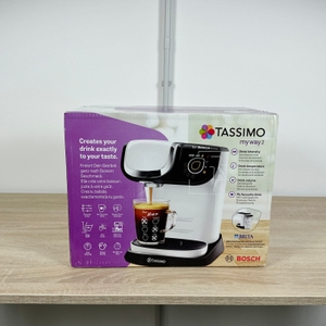 Die Verpackung der Bosch Tassimo My Way 2 steht auf einem Tisch. Vorderseite mit Produktabbildung und Funktionshinweisen ist gut erkennbar.