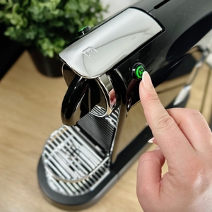 Eine Hand drückt die Ein-/Aus-Taste der De’Longhi Citiz. Das Gerät wird über einen runden Knopf an der Oberseite aktiviert.