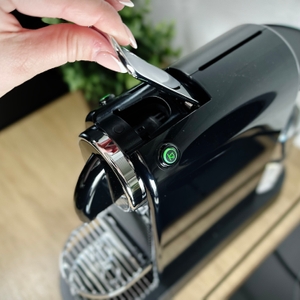 Eine Hand legt eine violette Nespresso-Kapsel in die De’Longhi Citiz ein. Der offene Mechanismus der Maschine ist gut sichtbar.