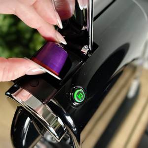 Eine Hand hält eine lila Nespresso-Kapsel über der De’Longhi Citiz. Die Maschine ist bereit für den nächsten Bezug.