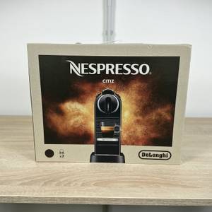 Die Verpackung der Nespresso De’Longhi Citiz steht auf einem Holztisch. Produktbild und Logo sind gut sichtbar.
