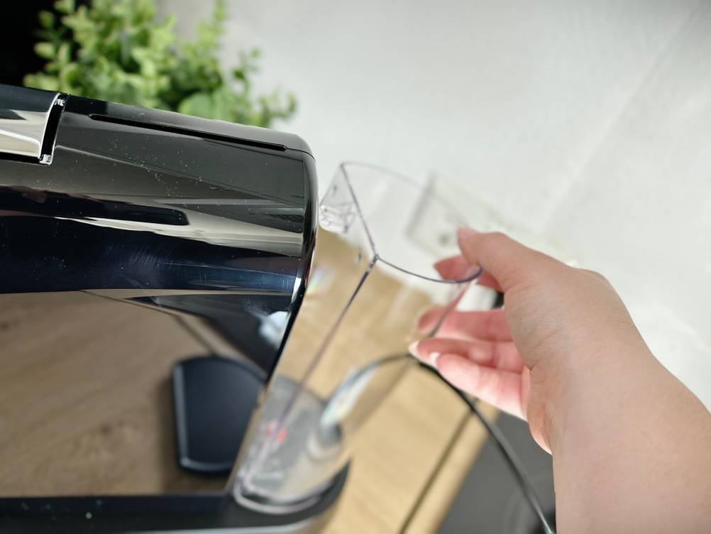 Eine Hand entfernt den Wassertank von der Rückseite der Nespresso Citiz. Der transparente Behälter wird nach oben abgezogen.