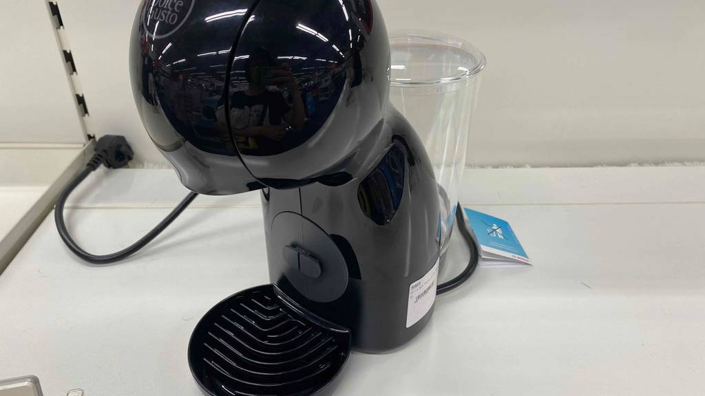 Die Kapselmaschine Dolce Gusto Nescafé steht seitlich auf einer weißen Oberfläche vor einem weißen Hintergrund.