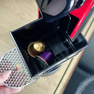 Gebrauchte Kapseln befinden sich im Auffangbehälter der Krups Nespresso XN7415 Citiz. Eine Hand zeigt den geöffneten Behälter.