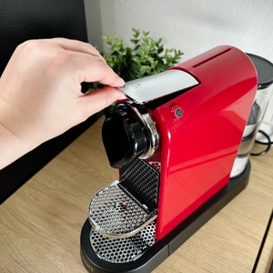 Eine Hand hebt den Hebel der Krups Nespresso XN7415 Citiz. Die Brühkammer ist geöffnet.