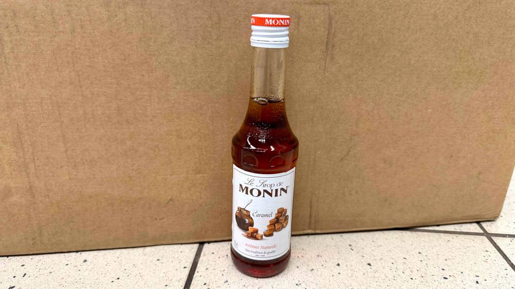 Karamell-Sirup im Test: Eine Flasche steht vor einem Karton auf dem Boden.