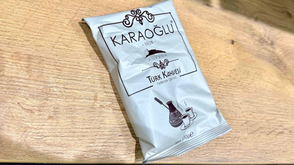 Eine 100-g-Packung mit getestetem türkischem Kaffee Ankara der Marke KARAOGLU liegt auf einer Holzfläche.