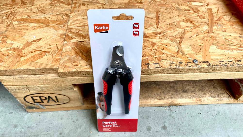 Krallenschere getestet: Ein Gerät in transparenter Originalverpackung lehnt an einer Holzpalette.