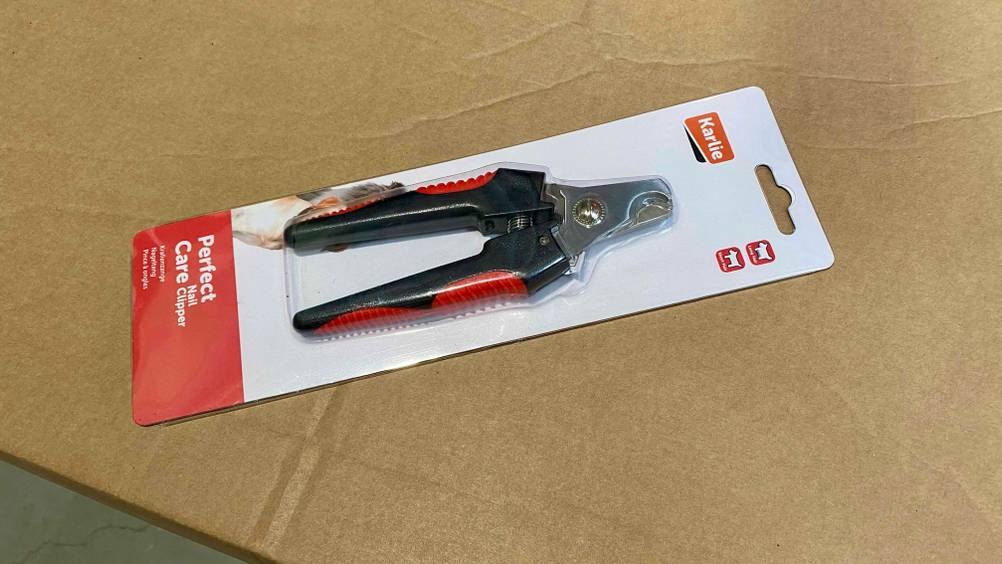 Eine getestete Krallenschere originalverpackt auf einem brauen Karton.