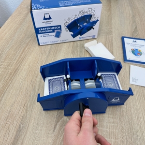 Eine Heldengut-Kartenmischmaschine wird per Handkurbel bedient, während zwei Kartenstapel im Inneren gemischt werden.