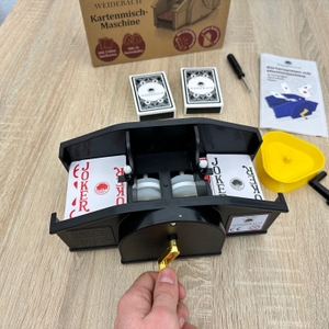 Eine Weidebach-Kartenmischmaschine mischt Spielkarten, während eine Hand die goldfarbene Kurbel betätigt.