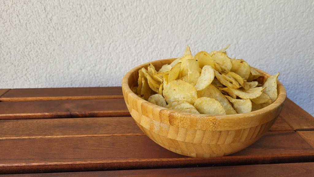 Auf einem Holztisch befindet sich eine Schüssel gefüllt mit getesteten Kartoffelchips.