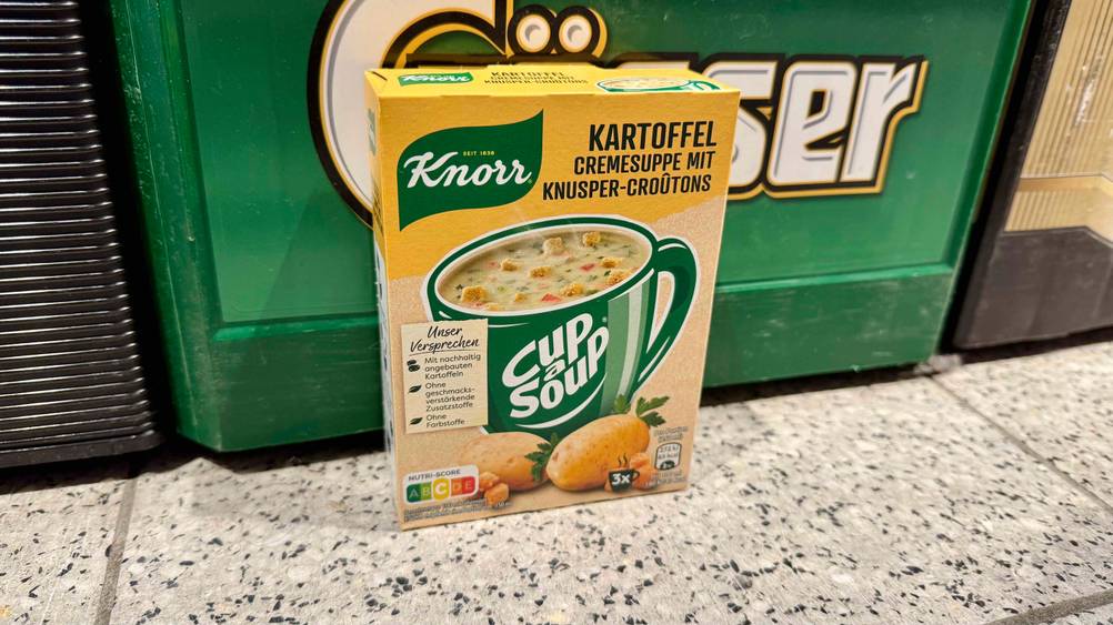 Vor einem Getränkekasten steht eine Kartoffelsuppe im Test auf dem Boden.