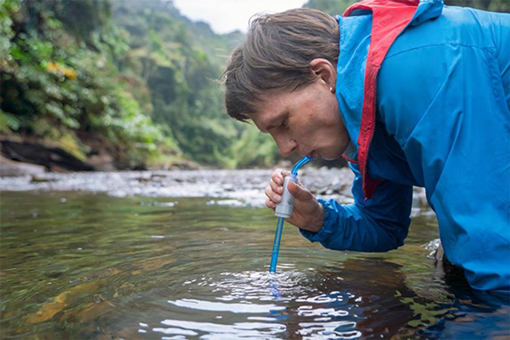 Katadyn-Wasserfilter im Test: Ein Mann, der mit einem Schnorchel-Wasserfilter direkt aus der Wasserquelle trinkt.