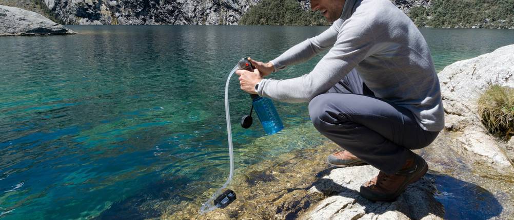 Katadyn-Wasserfilter im Test: Ein Mann, der einen Wasserfilter an einem öffentlichen Gewässer nutzt.