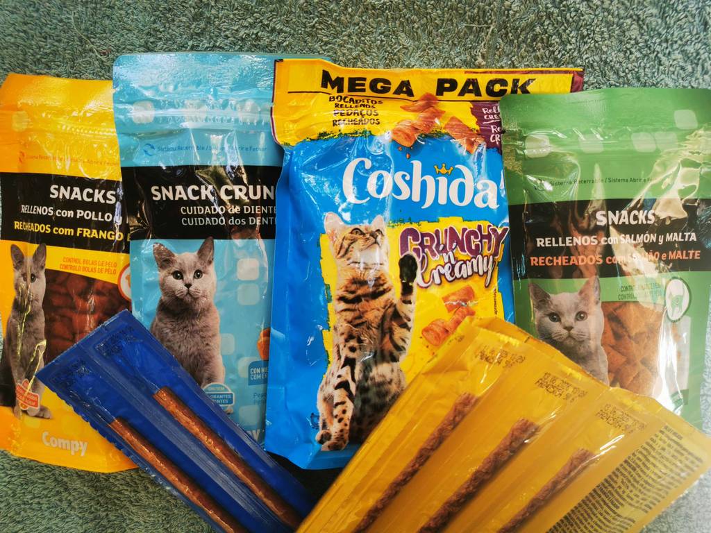 Mehrere Packungen verschiedener Katzenleckerlies liegen zu testen auf einer Frotteeunterlage.