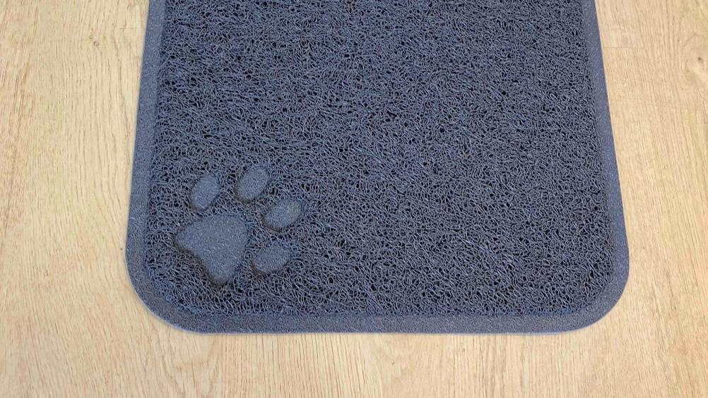 Nahaufnahme eines Pfotenabdrucks auf einer getesteten Katzenstreu-Matte auf einer Holzfläche.