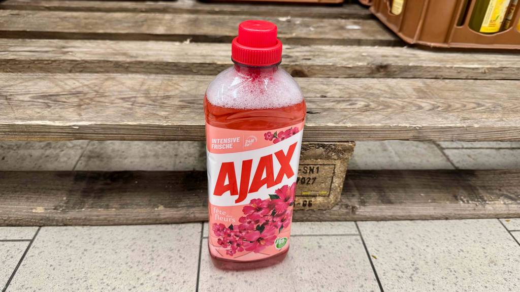 Ajax-Allzweckreiniger im Test: Eine Kunststoffflasche mit roter Flüssigkeit steht vor einer Holzpalette.