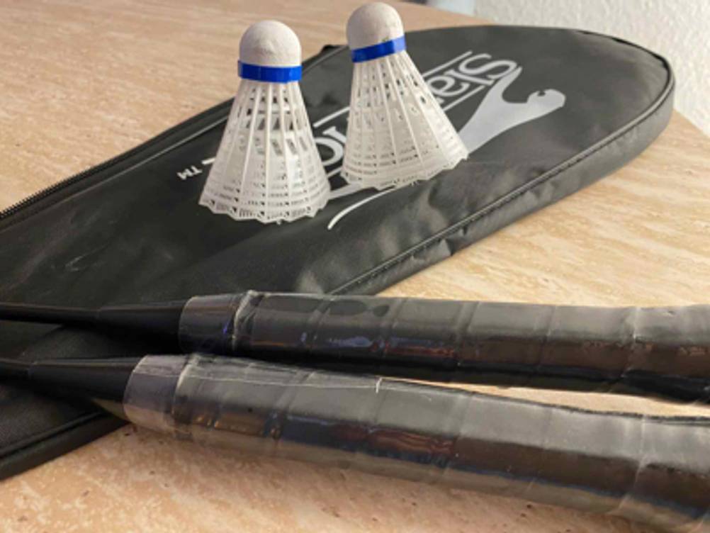 Ansicht zweier Schägergriffe des Federball-Sets im Test liegend über einer schwarzen PVC- und Stofftragetasche, auf der zwei Federbälle stehen.
