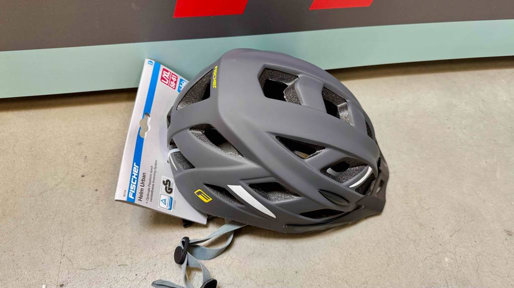 Im Test: Ein Fischer-Fahrradhelm in Schwarz liegt vor einem Regal.