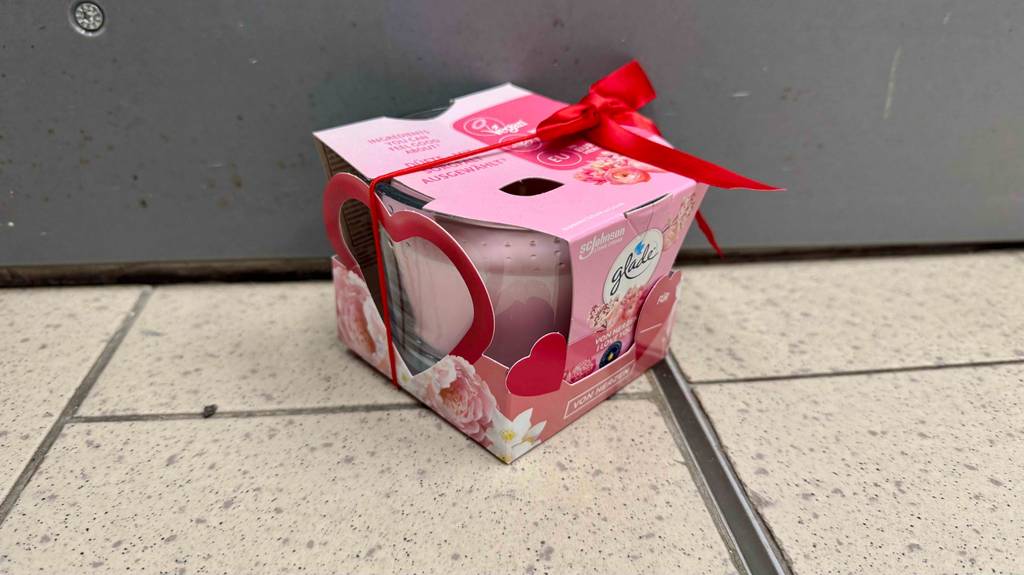 Eine Verpackung mit einer rosafarbenen, getesteten Glade-Duftkerze steht auf dem Boden.