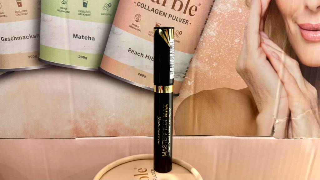 Max-Factor-Mascara Test: Ein schwarzer Stift steht vor einem Kosmetikplakat.