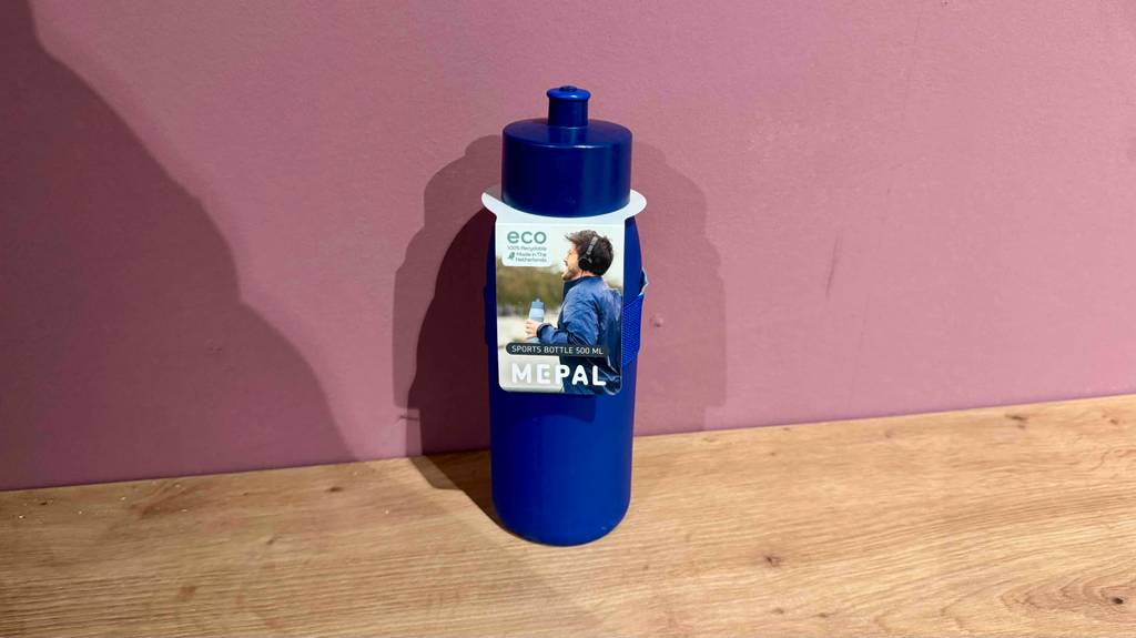 Eine getestete Mepal-Trinkflasche in Blau steht auf dem Boden vor einer rosafarbenen Wand.