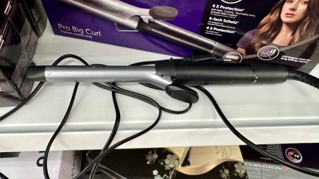 Der getestete Remington-Lockenstab liegt auf einem weißen Regal im Verkaufsbereich vor seiner Verpackung.