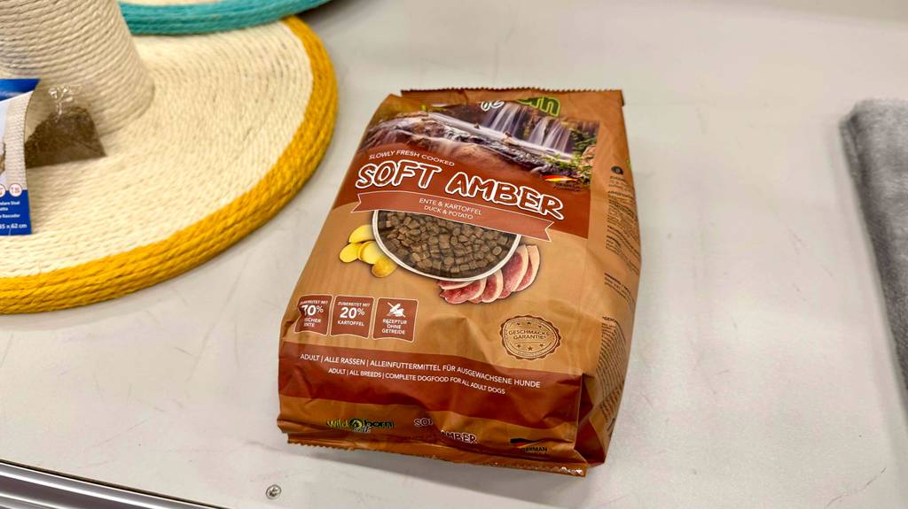 Wildborn-Hundefutter im Test: Eine braune Packung mit Soft Amber Trockenfutter liegt auf einem Regal neben einem Sonnenhut.