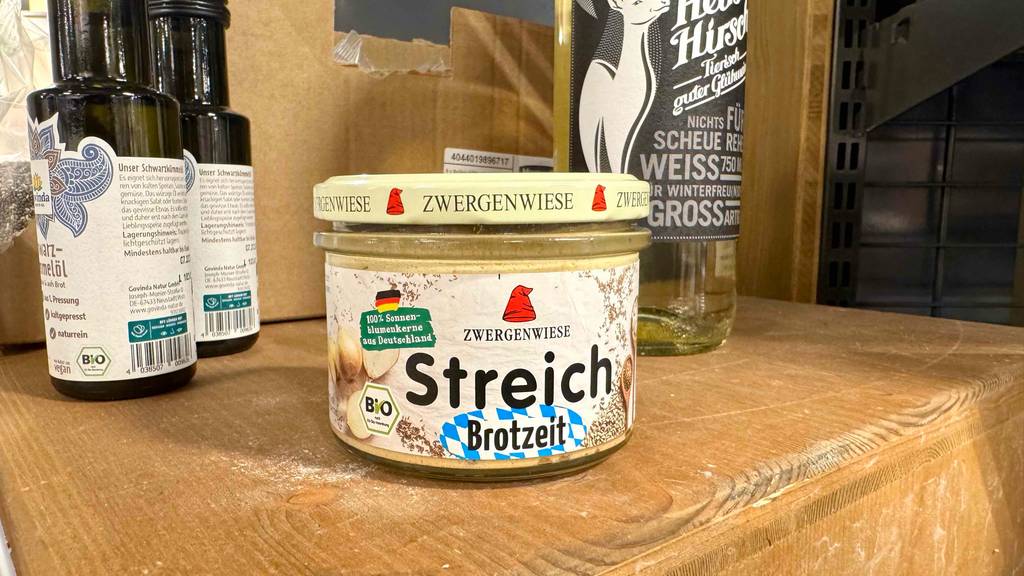 Ein getesteter Zwergenwiese Brotaufstrich befindet sich im Glas mit Schraubverschluss auf einem Holzregal im Geschäft.