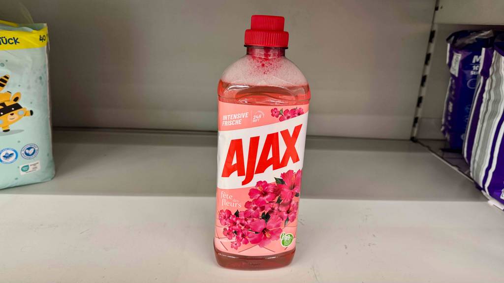 Ajax-Allzweckreiniger-Test: Eine Kunststoffflasche mit roter Flüssigkeit steht auf einem weißen Regal.