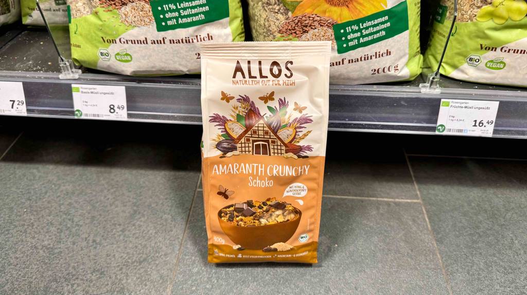 Eine 400-g-Tüte mit getestetem Allos Müsli steht vor einem Verkaufsregal auf dem Boden.