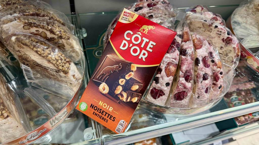 Getestet: Côte d’Or-Schokolade in der roten Verpackung mit Nüssen liegt in einem Verkaufsregal auf süßen Kuchen.