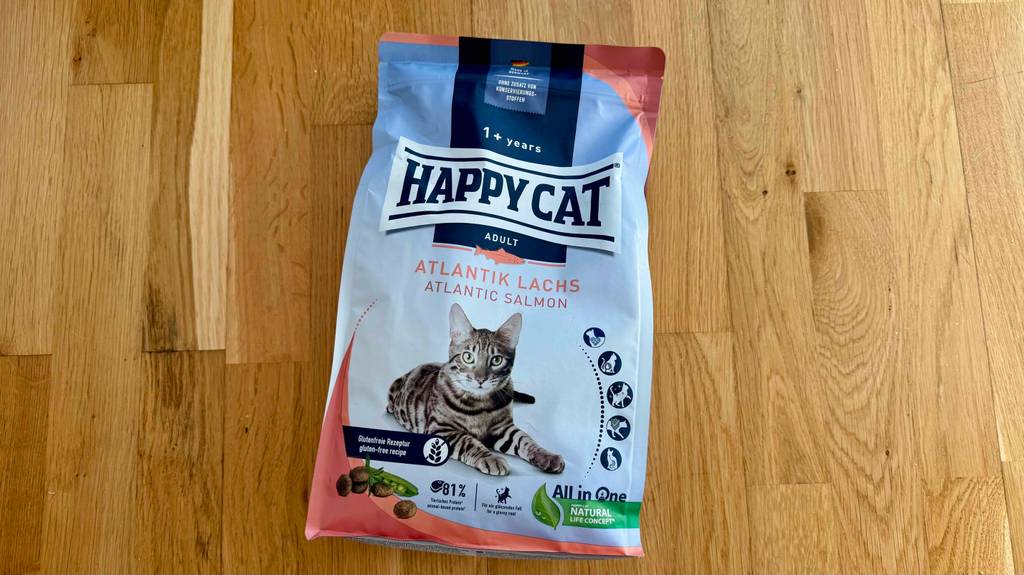 Eine Portionstüte mit Happy Cat Katzenfutter im Test liegt auf einem Holzboden.
