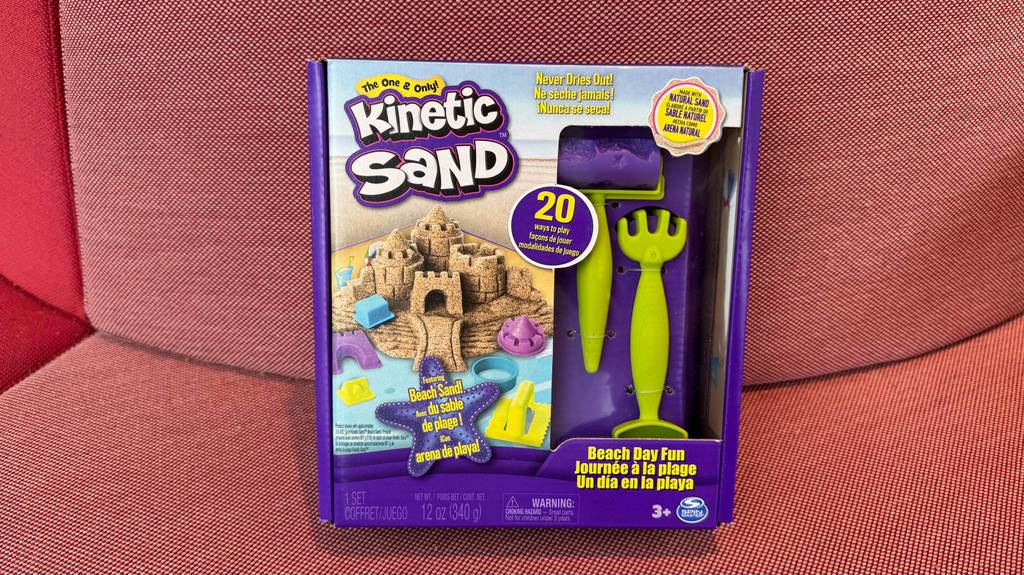 Im Test: Kinetic Sand in der Originalverpackung inklusive Zubehör steht auf einem roten Sessel.