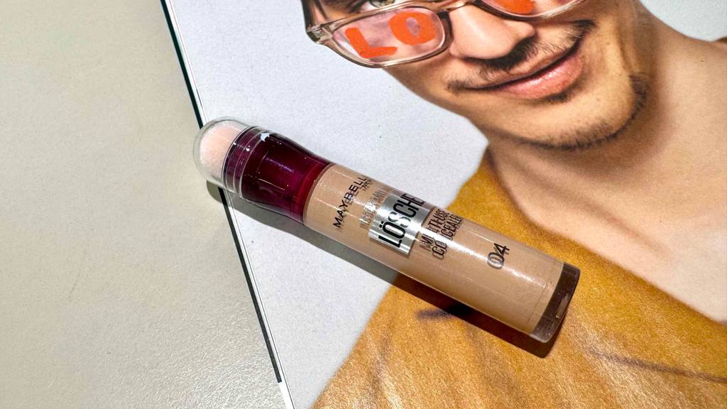 Ein getesteter Maybelline-Concealer liegt auf einem Drogeriemarktplakat.