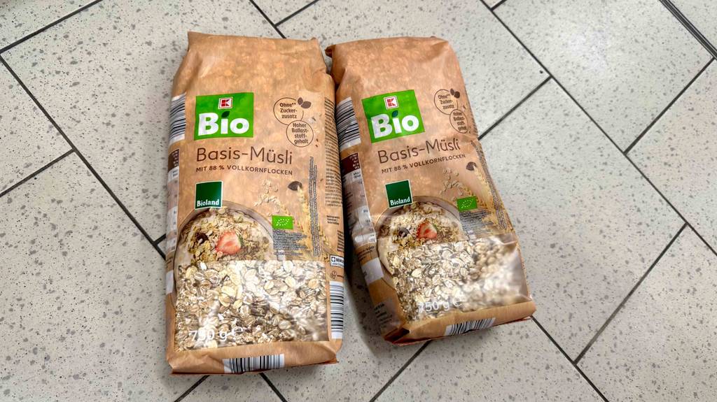 Bio-Müsli Test: Zwei 750-g-Packungen mit Sichtfenstern liegen auf einem Fliesenbelag.