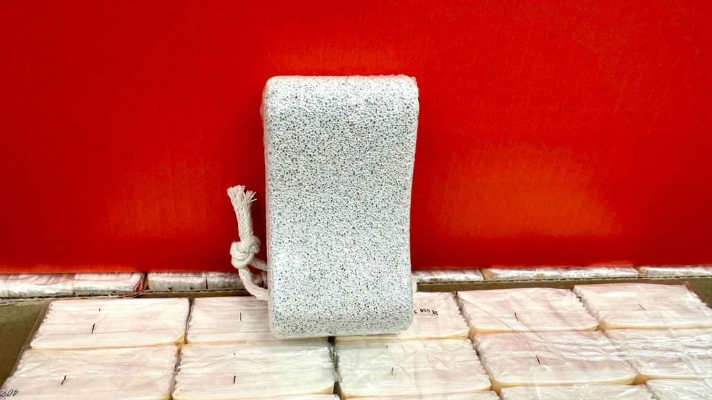 Ein weißer Bimsstein im Test inklusive Kordel zum Aufhängen steht vor einem roten Karton.