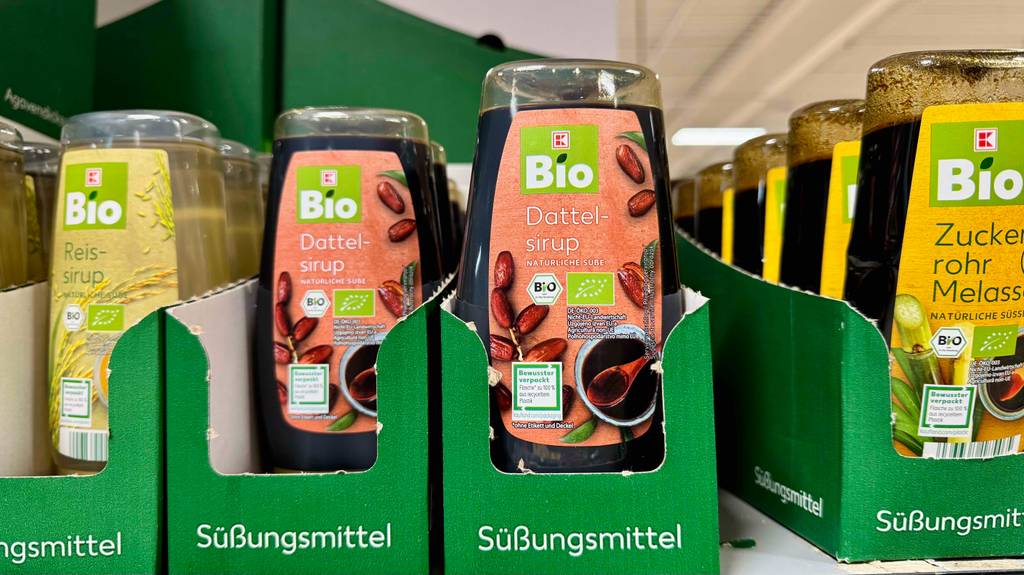 Getesteter Dattelsirup in der Quetschflasche befindet sich in einem Karton neben weiteren Sirup-Produkten im Supermarkt.