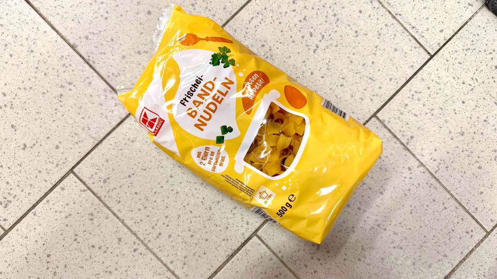 Eine gelbe 500-g-Packung getesteter Bandnudeln der Marke Kaufland liegt auf einem Fliesenboden.