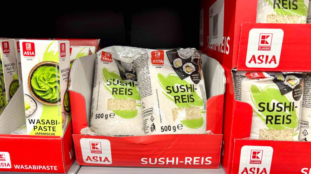 Sushi-Reis-Test: Mehrere 500-g-Packungen mit Sichtfenstern befinden sich in Kartons auf einem Verkaufsregal.