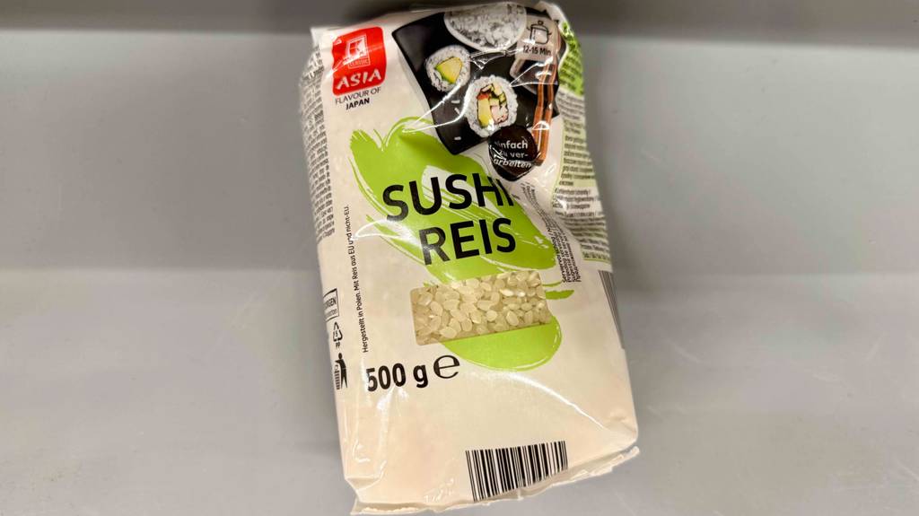 Eine 500-g-Packung mit Sichtfenster, hinter dem getesteter Sushi-Reis ersichtlich ist, liegt auf einer weißen Oberfläche.