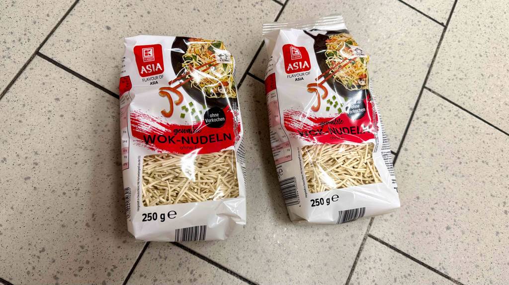 Im Test: Wok-Nudeln in zwei 250-g-Packungen, die auf einem Fliesenboden liegen.
