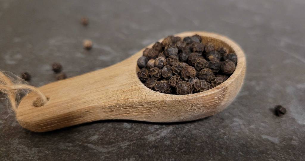 Getesteter schwarzer Pfeffer liegt auf einem Holzlöffel.