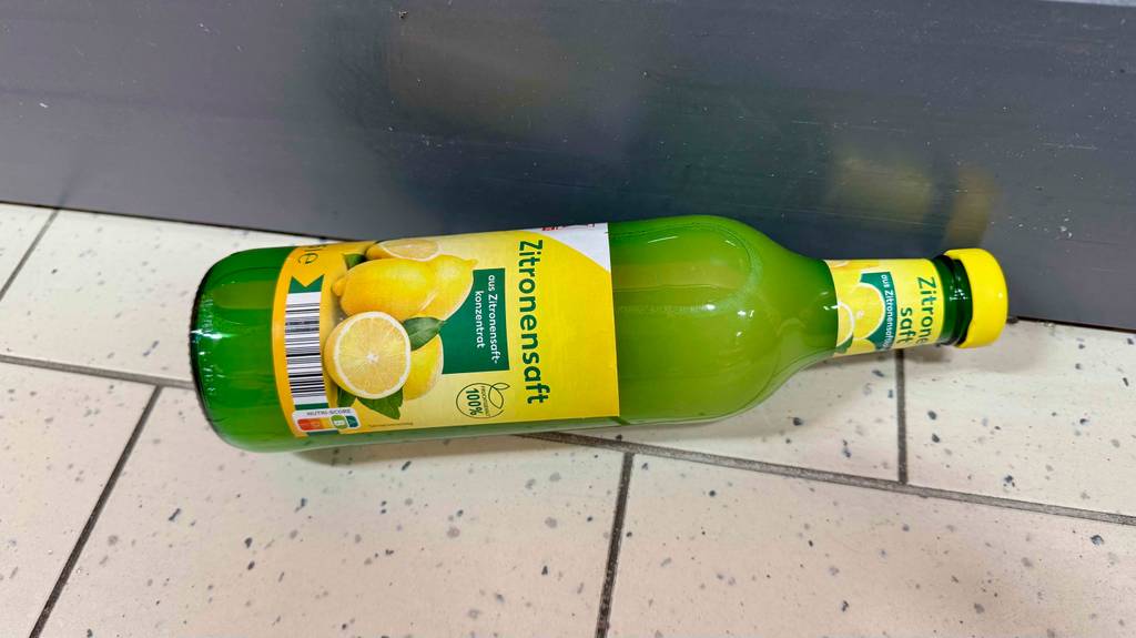 Eine Glasflasche mit getestetem Zitronensaft liegt auf dem Boden.