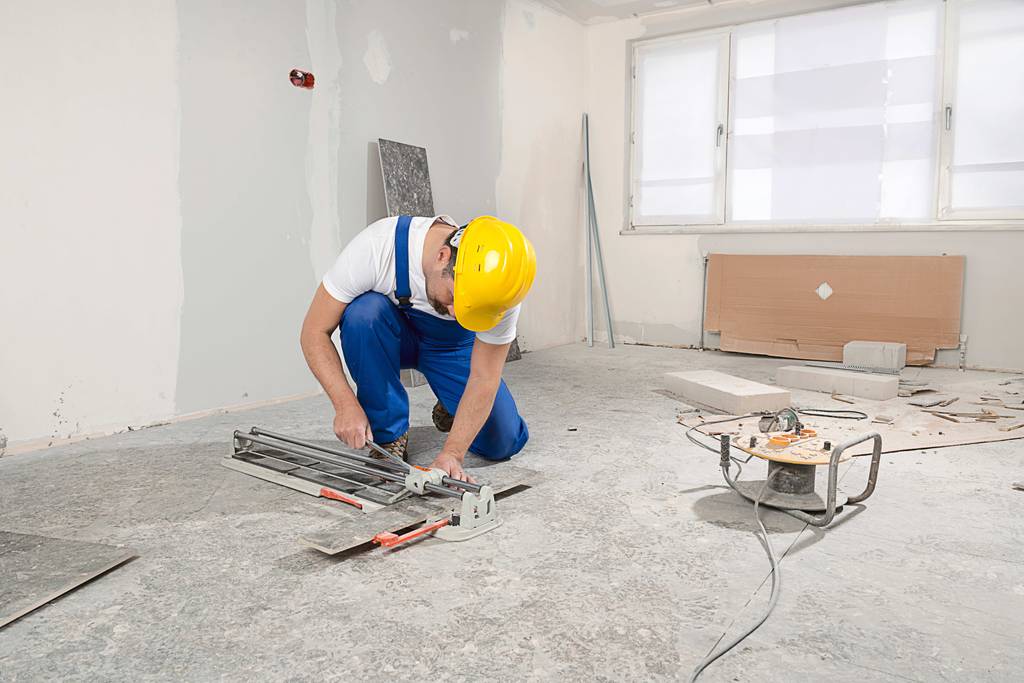 Kaufmann-Fliesenschneider im Test: Ein Mann mit Helm schneidet auf einer Baustelle auf dem Boden eine breite Fliese.