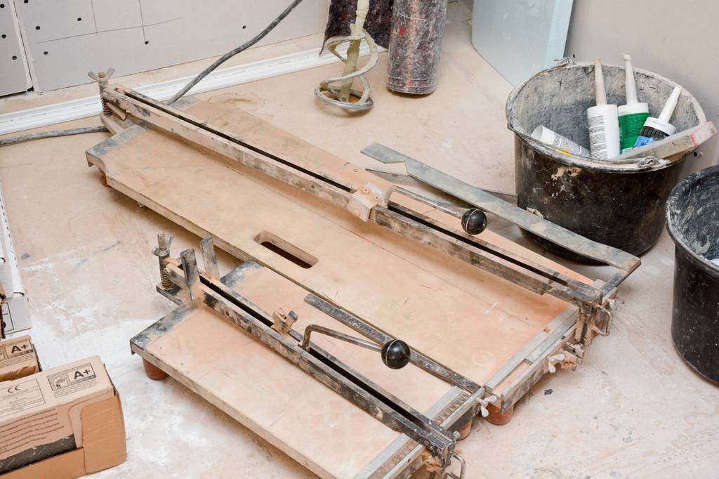 Kaufmann-Fliesenschneider im Test: Zwei unterschiedlich große Fliesenschneider stehen nebeneinander auf dem Boden, darum herum Eimer, Kartuschen und Werkzeug.