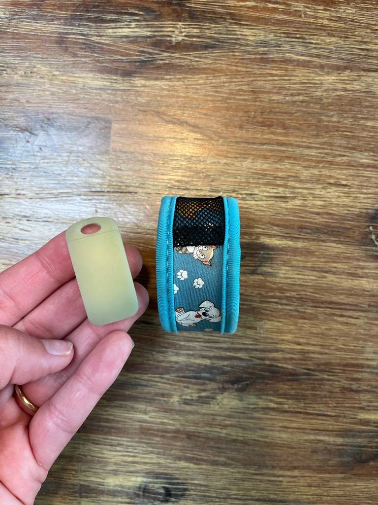 Eine Hand hält den auswechselbaren Geruchschip neben ein getestetes Mückenband in Türkis.
